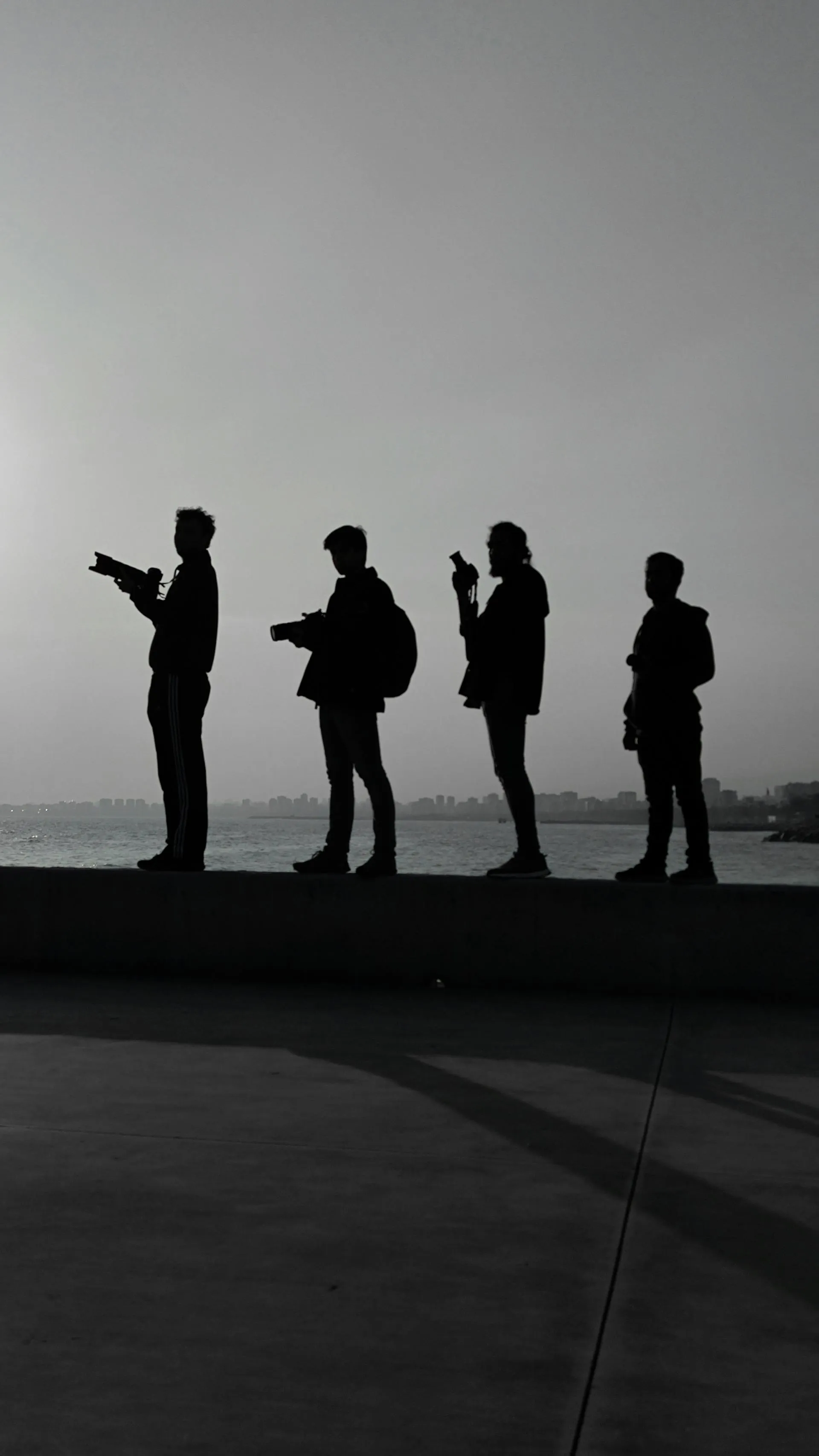 Four silhouetted figures holding cameras and phones on a waterfront