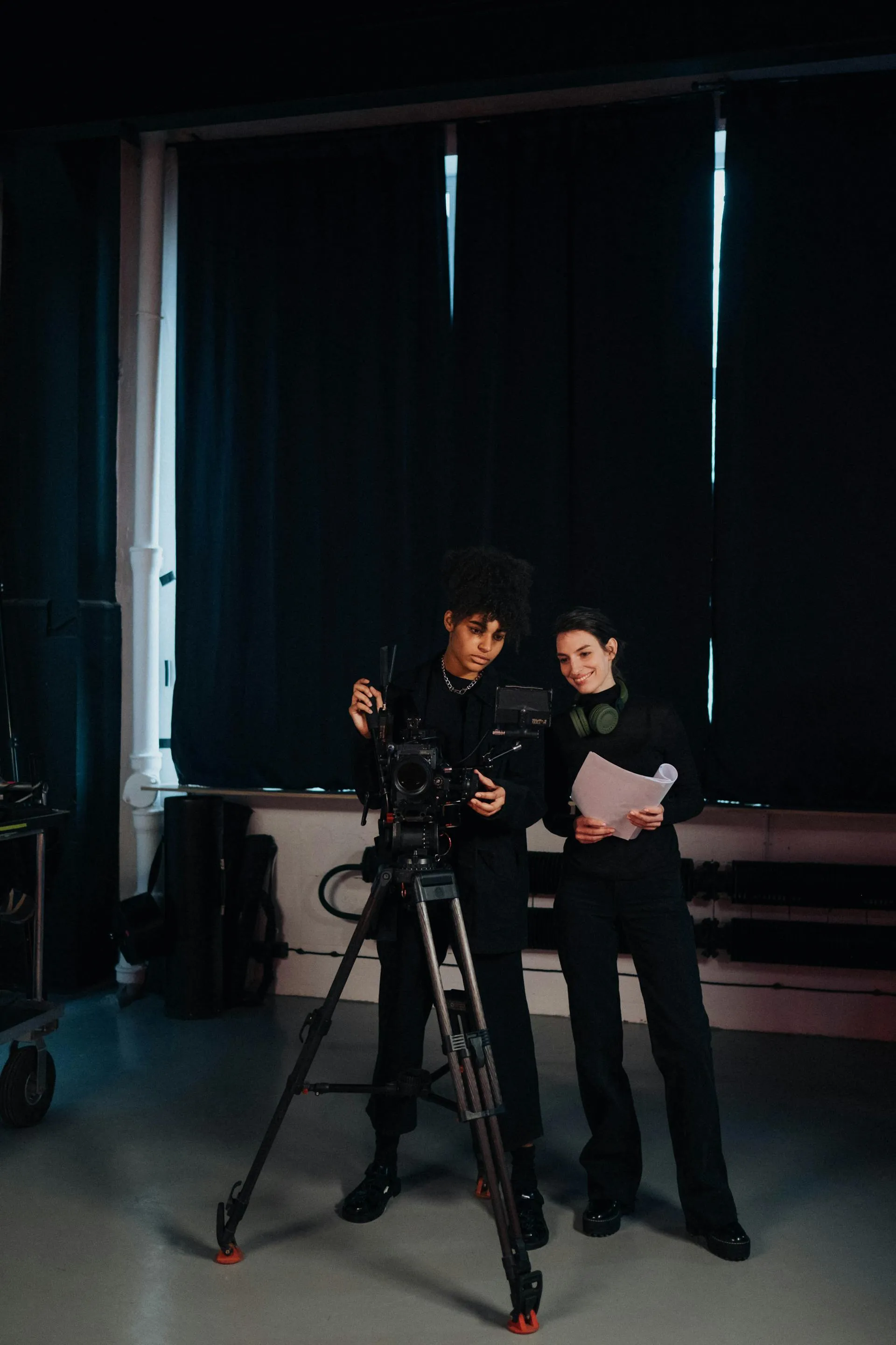 Two crew members reviewing a shot on a tripod-mounted camera in a dark studio