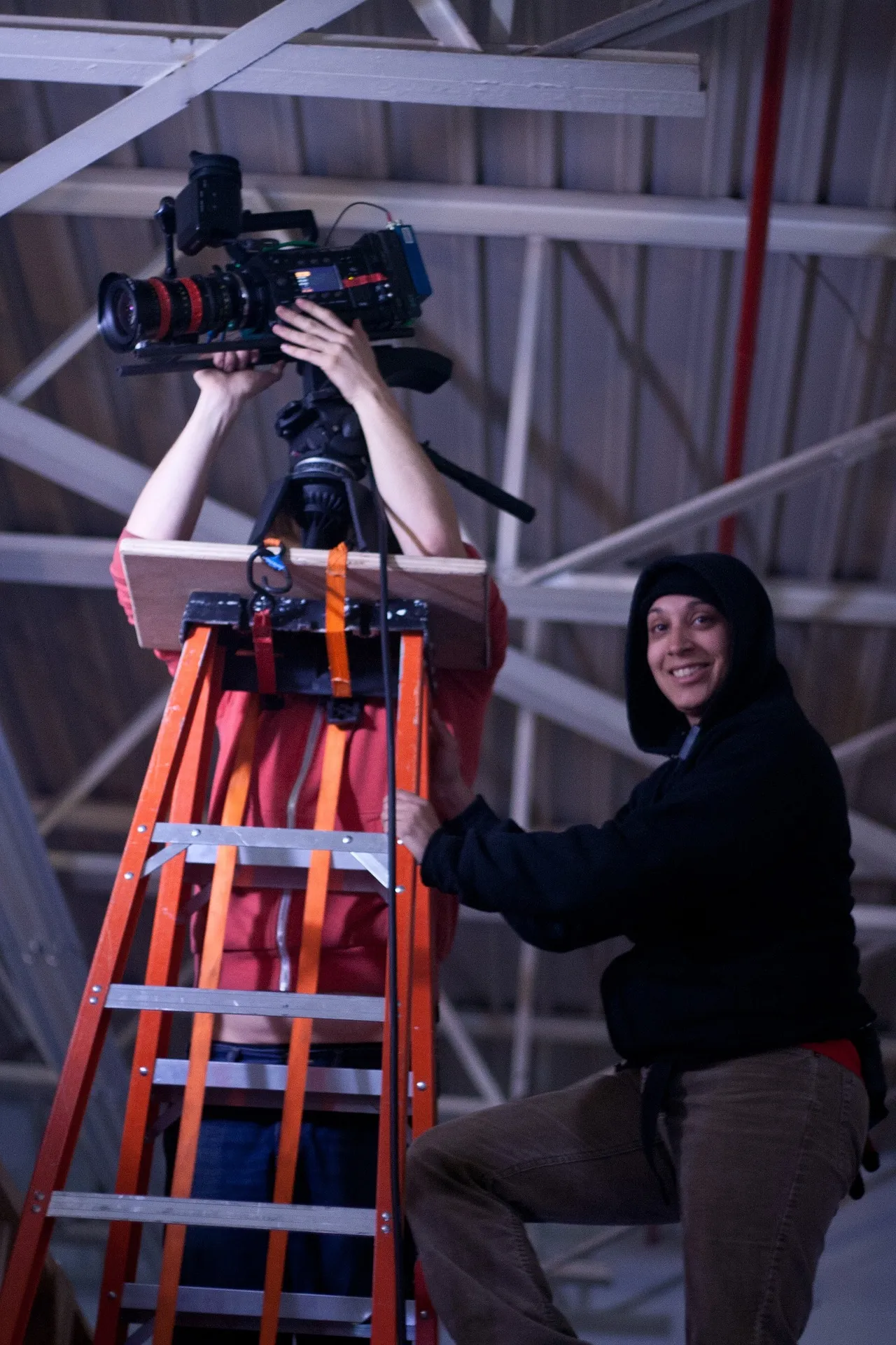 A production crew filming on location, camera operator on a ladder framing a shot
