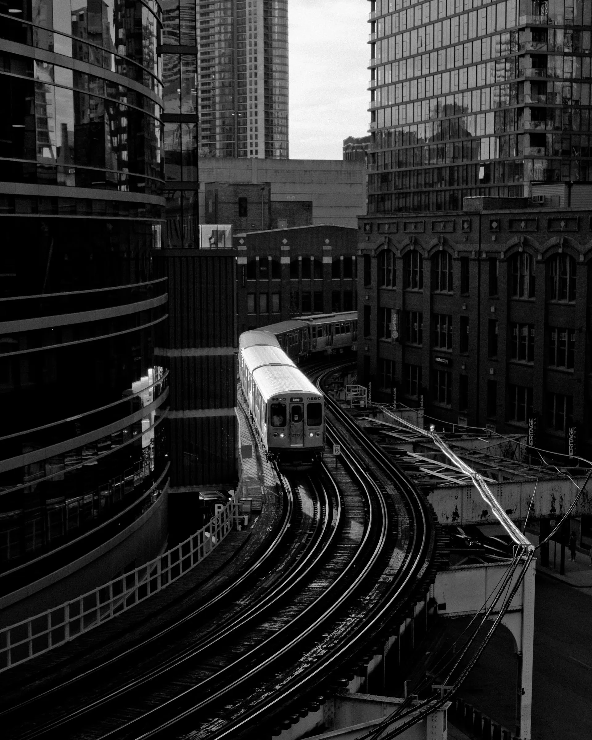 A black-and-white photo of a Chicago elevated train curving between buildings