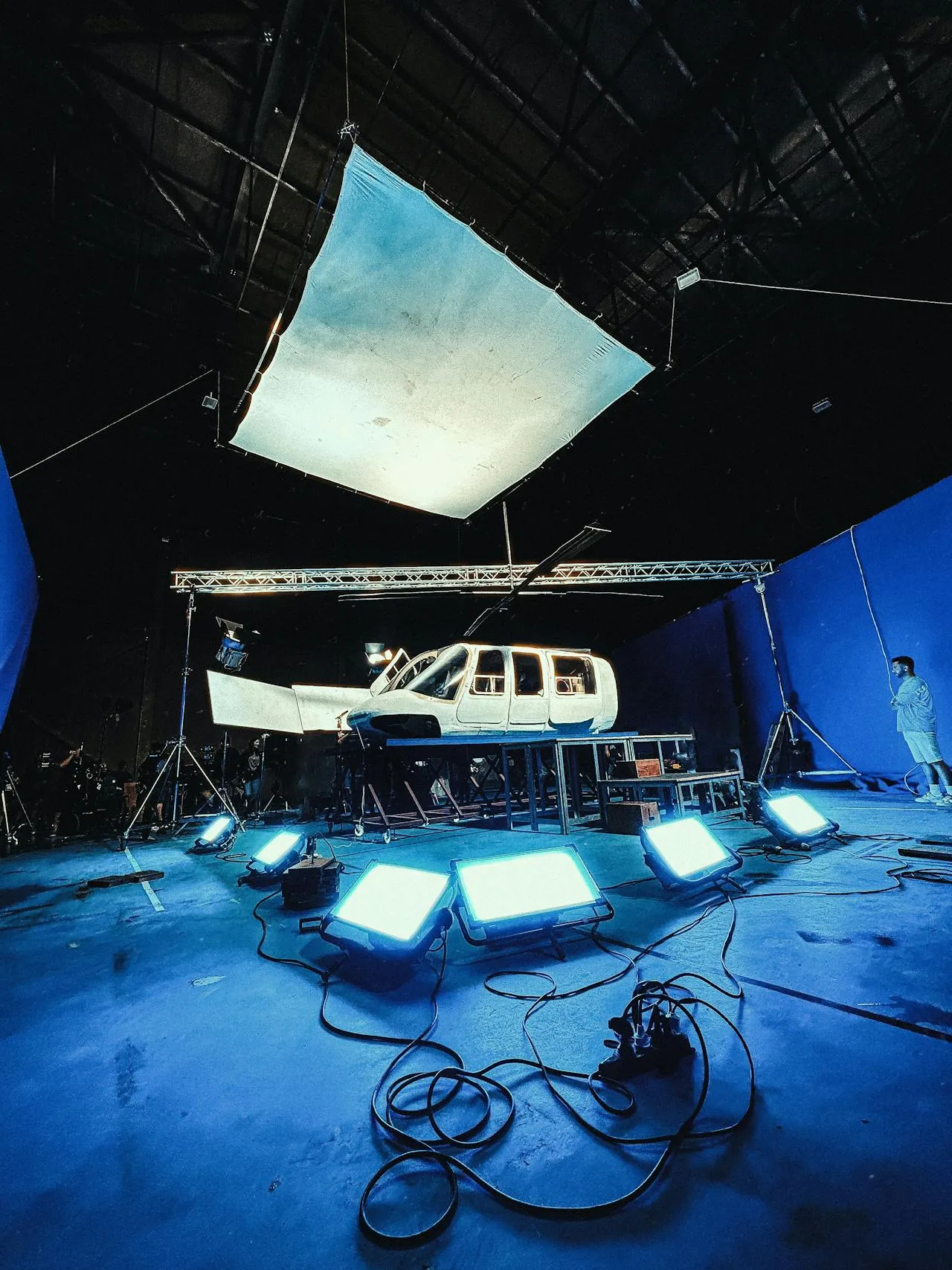 A vehicle rigged for a shoot on a blue-lit soundstage surrounded by lighting equipment